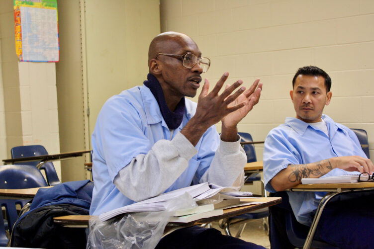 Two students seated at desks in a classroom participating in a discussion.