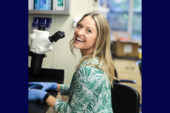 A smiling woman sits at a microscope