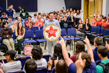 Marching Illini director Barry Houser holds a drum top with the Macy's Thanksgiving Day Parade logo while band members cheer.
