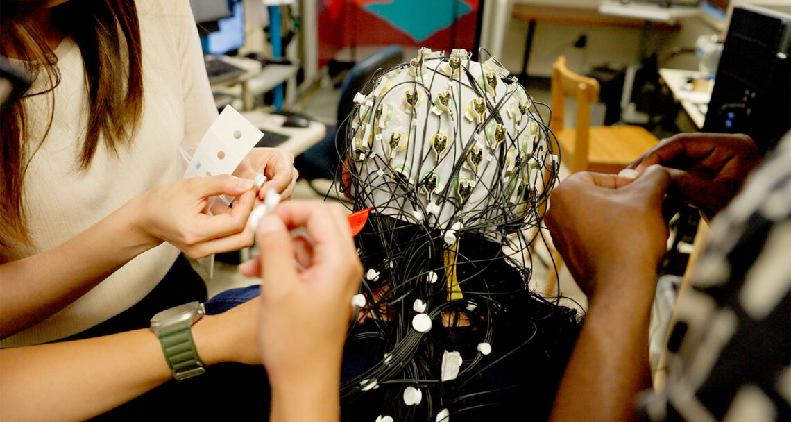 View of cap placement from the back of a participant's head. Several people are setting up the individual electrodes for attachment.