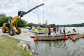 photo of a crane unloading two floating wetland structures into Lake Decatur.
