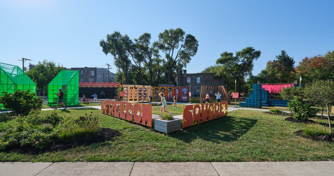 Photo of a park with letters spelling out "Freedom Square," children playing and various structures in the background.