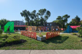 Photo of a park with letters spelling out "Freedom Square," children playing and various structures in the background.