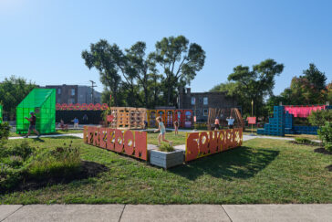 Photo of a park with letters spelling out "Freedom Square," children playing and various structures in the background.