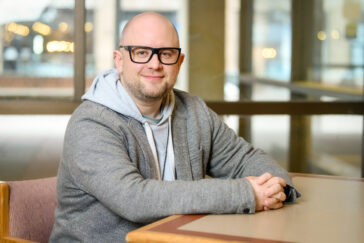 Photo of Benedek Kurdi seated at a table in front of a bay of windows.