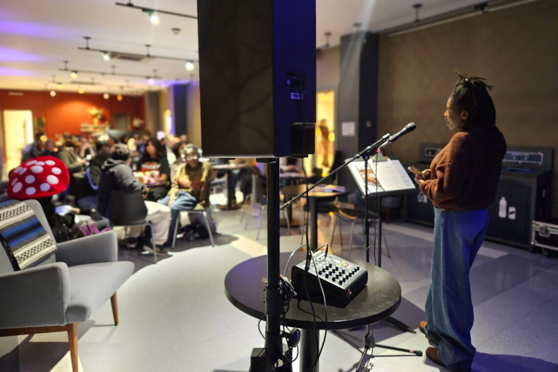 Photo of a woman standing in front of a microphone and music stand, facing a seated group of people.