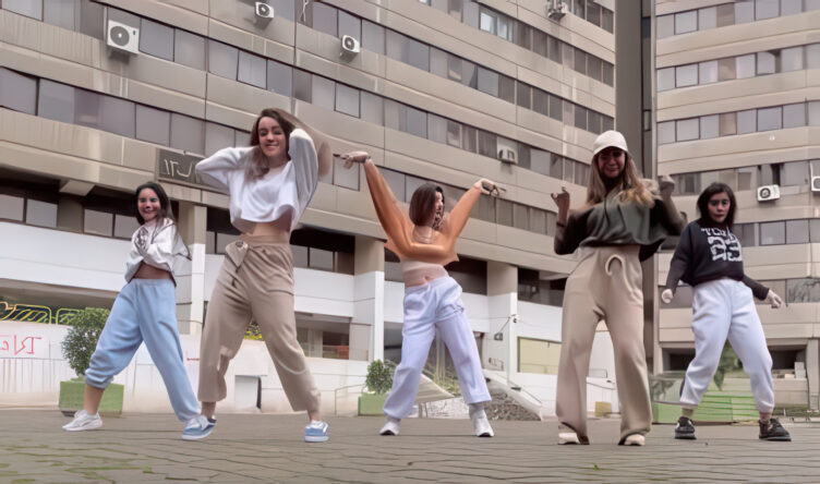 Five young women dancing unveiled in a public courtyard with high-rise buildings behind them in Ekbatan.
