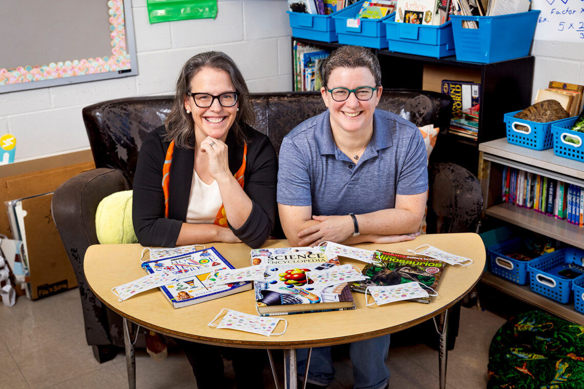 Portrait of the researchers in a classroom. They are seated at a child-sized table with educational materials spread across it.