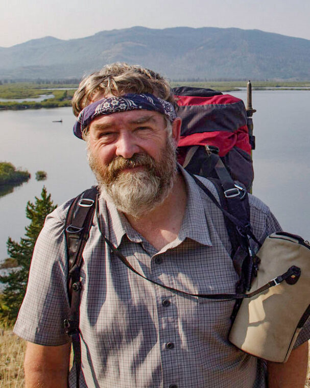Photo of Bob Pahre wearing a backpack and standing in front of a lake in Yellowstone National Park.