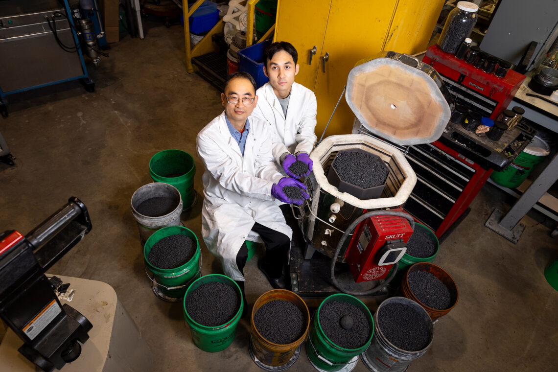 Photo of researchers seated next to kiln and multiple buckets of pelletized biochar.