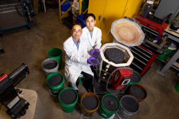 Photo of researchers seated next to kiln and multiple buckets of pelletized biochar.