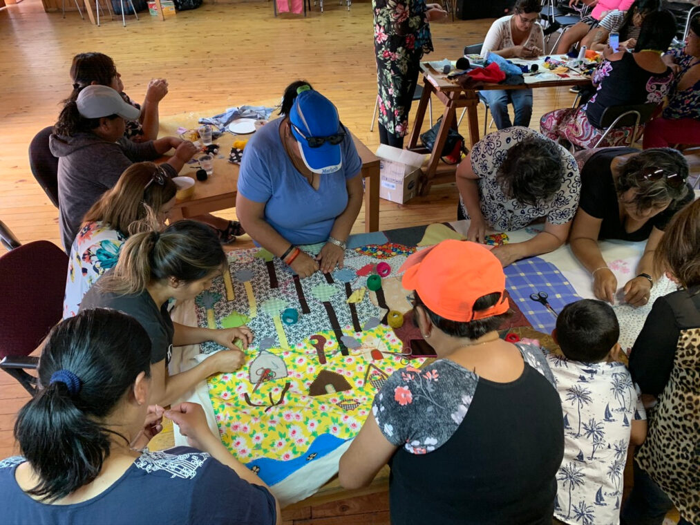 Photo of women from Lota, Chile working on an arpillera depicting scenes from their city.