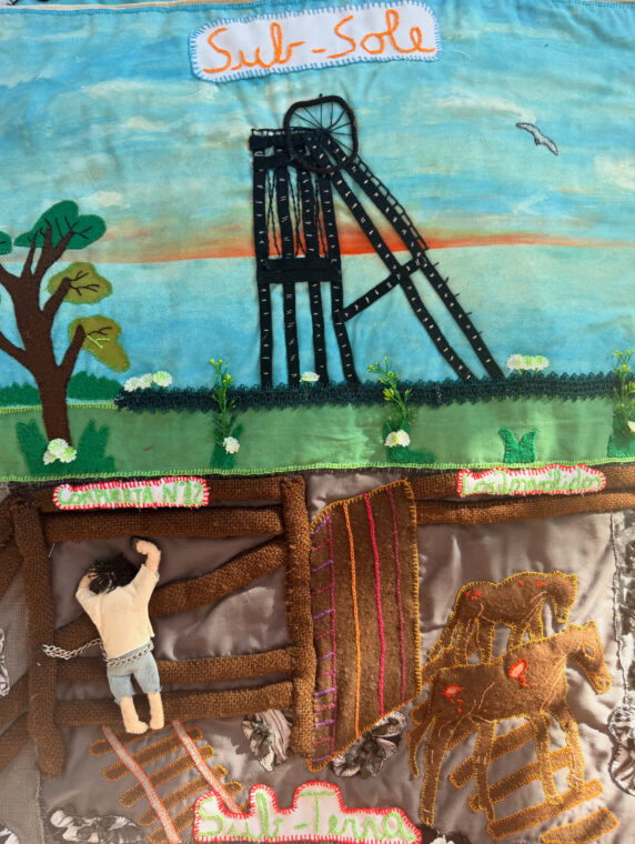 Photo of an arpillera showing scenes of coal mining.