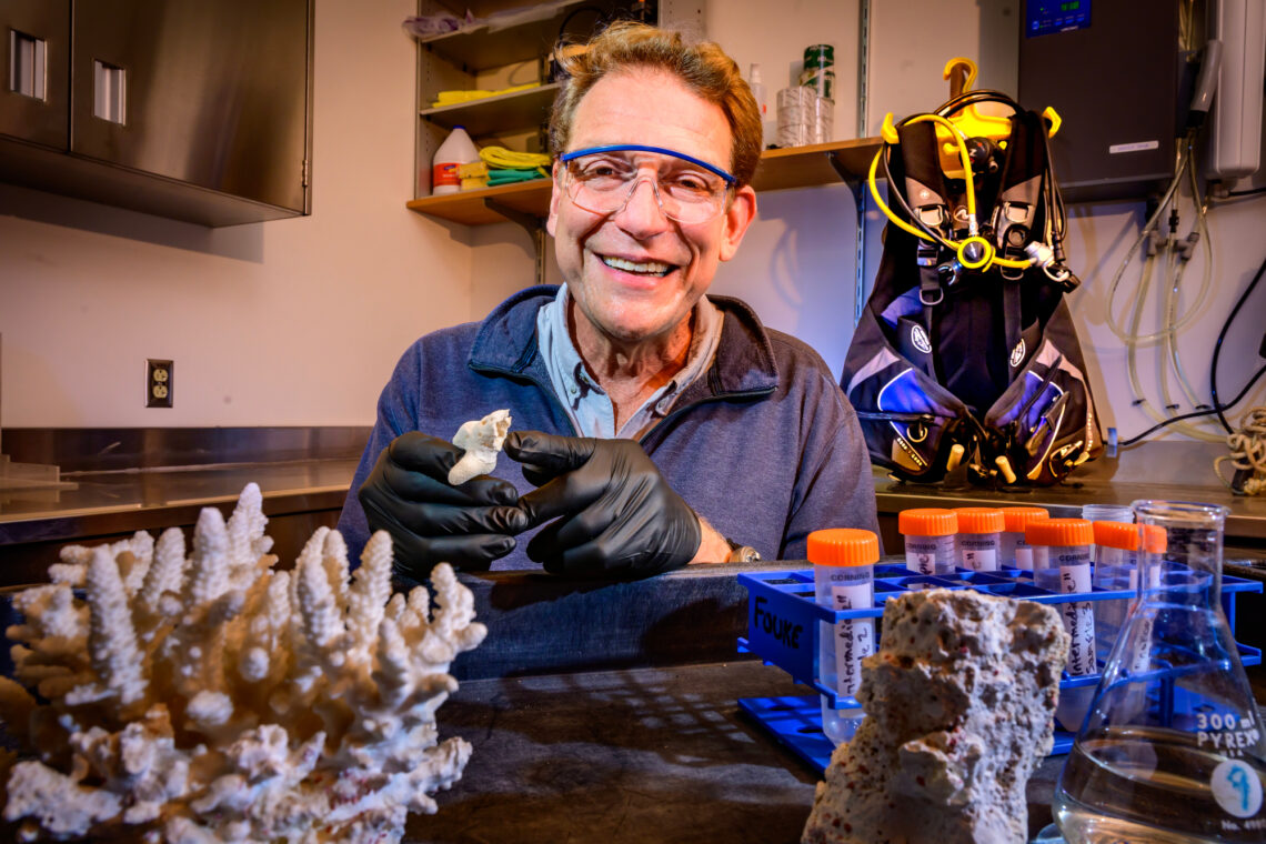 Photo of Bruce Fouke in a laboratory. He is holding a hollowed-out coral branch in gloved hands. 