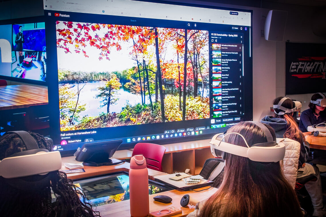 Photo of a student wearing virtual reality goggles with a screen showing a wilderness photo in the background.
