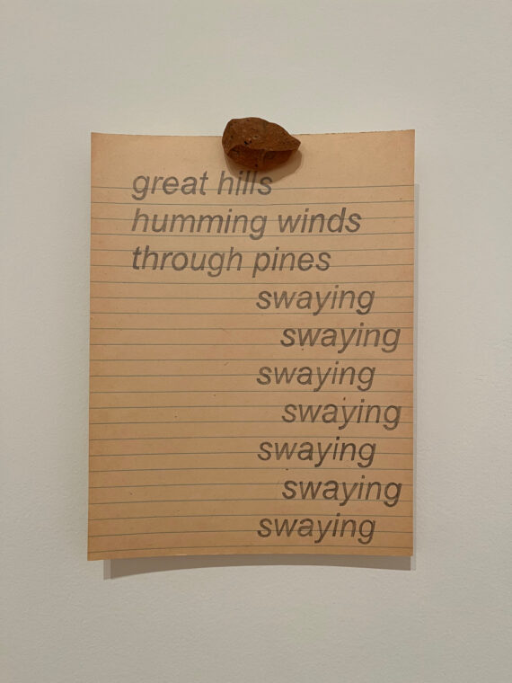 Photo of a paper with poetry written to mimic typeface and fastened to the wall with a rock.