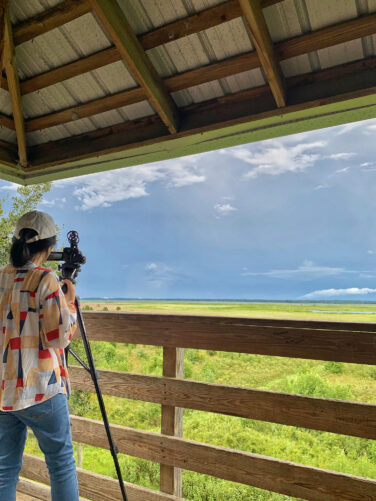 Lu standing on an observation platform with a video camera recording the landscape.