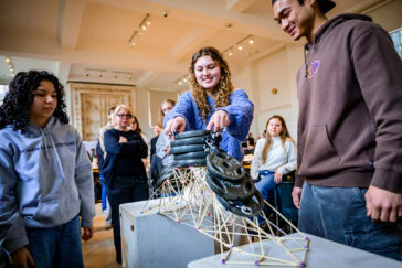 Photo of a student placing weights on top of a bamboo stick truss while other students watch.