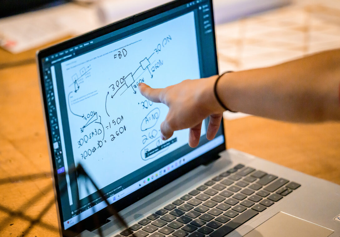 Photo of a hand with a finger pointing at an equation on a computer screen.