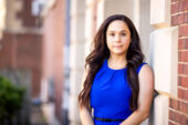 Photo of Rachel Hoopsick standing in a blue dress outside a university building.