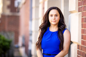 Photo of Rachel Hoopsick standing in a blue dress outside a university building.