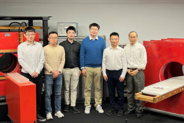 Six people stand in front of red MRI machines