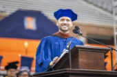 A man, Sean Evans, in graduation regalia delivering a Commencement speech