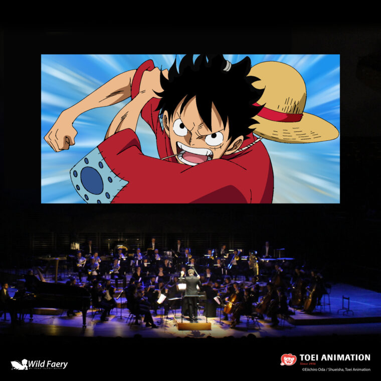 Photo of a large screen with an image from Japanese anime, with an orchestra performing below the screen.