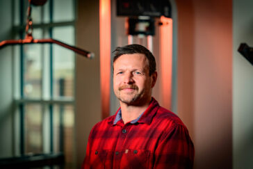 Photo of researcher in the gym. He is standing in front of a strength training machine.