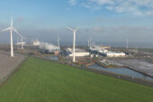 A photo of a large data center in a rural setting with cooling towers and windmills,