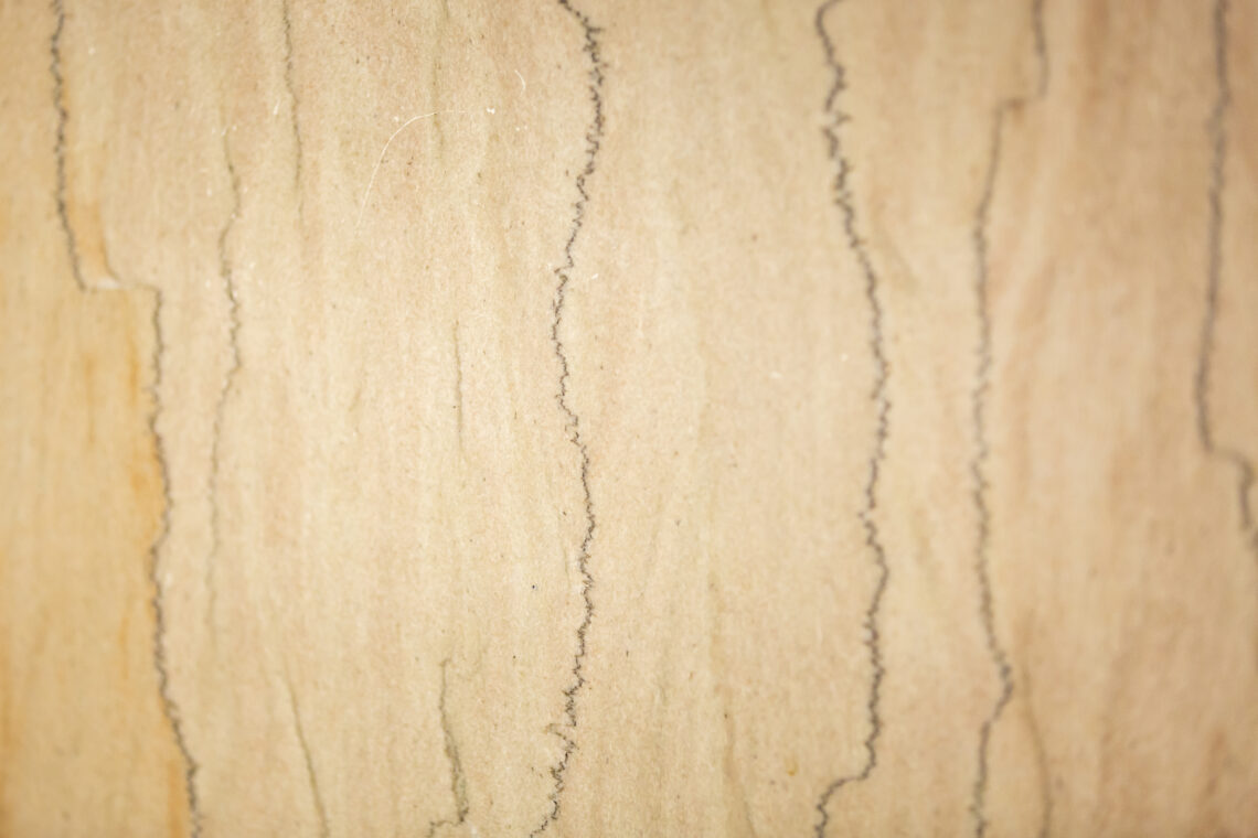 Closeup of a smooth limestone wall that is pinkish and yellowish, with jagged vertical red or black lines.