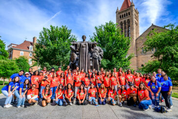 A large group of people stands by the Alma Mater statue