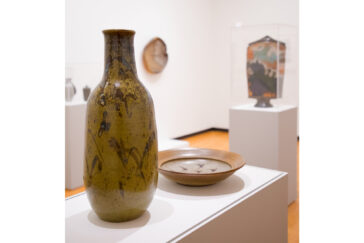 Photo of a tall gold ceramic vessel and a brown ceramic bowl decorated with abstract birds on display at Krannert Art Museum.