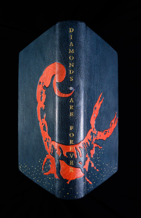 A photo of the cover of “Diamonds are Forever,” featuring a scorpion design, gilt grains of sand and a small diamond chip on the spine.