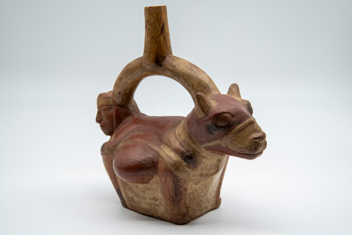 Photo of a ceramic vessel with two faces, one on either side, and a spout on top.