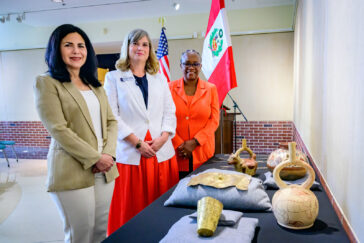 Photo of Verónika Bustamante Gómez, Elizabeth Sutton and Venetria Patton standing before a table with Peruvian objects at the museum.