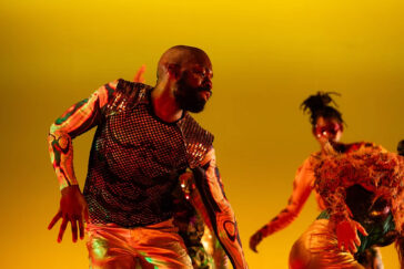 Photo of a dancer in a colorful costume with a mesh top.