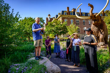 Rob Kanter on a rock in the Pleistocene Garden, with a group of people around him listening.